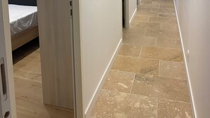 Ein Flur mit einem Bett im linken Zimmer, einer Tür zu einem weiteren Raum und einem gerahmten Bild an der Wand.