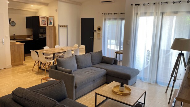 Ein modernes Wohnzimmer mit einem grauen Ecksofa, einem Couchtisch und einem Essbereich mit weißem Tisch und Stühlen.
