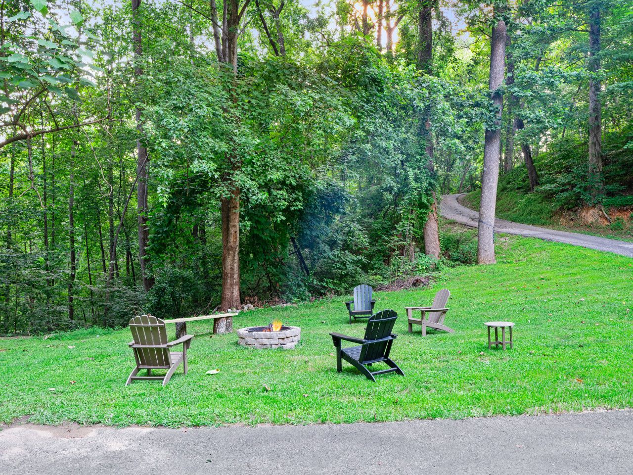 A grassy outdoor area with Adirondack chairs, a fire pit, and a bench.