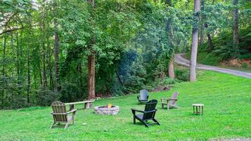 A grassy outdoor area with Adirondack chairs, a fire pit, and a bench.