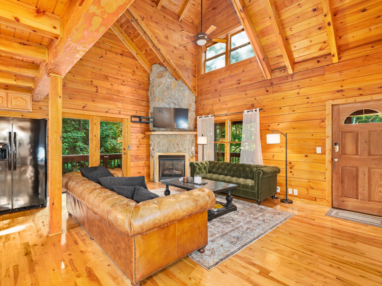 A wooden cabin interior with a stone fireplace, leather sofa, and a dining area.
