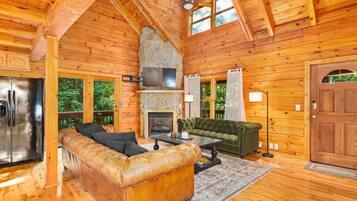 A wooden cabin interior with a stone fireplace, leather sofa, and a dining area.