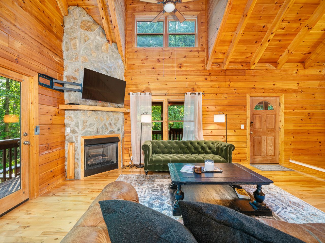 Ein Innenraum einer Blockhütte mit Kamin aus Stein, einem grünen Sofa, einem Holztisch und einem an der Wand befestigten Fernseher.