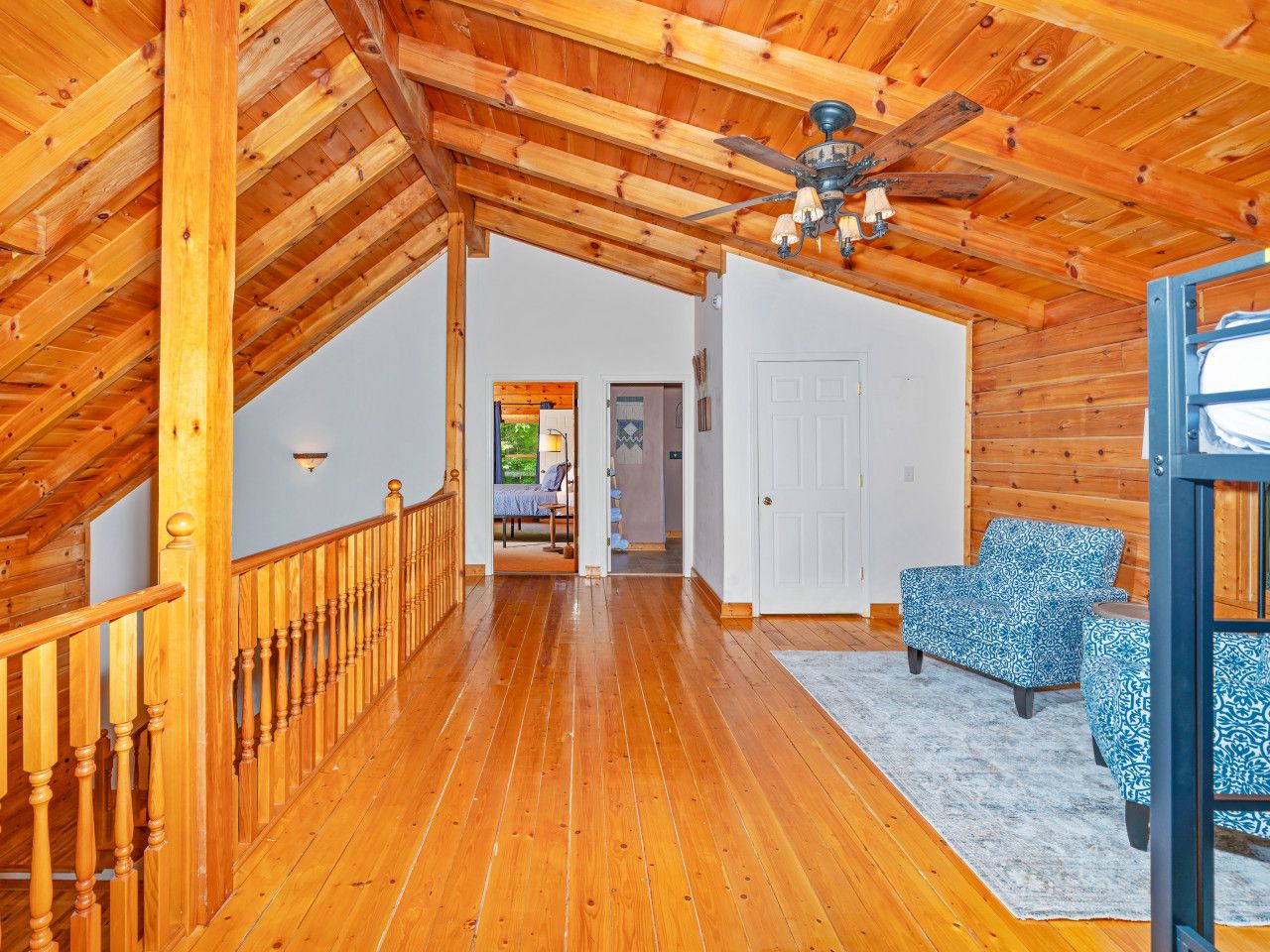 A wooden interior with a staircase, a ceiling fan, and patterned chairs.