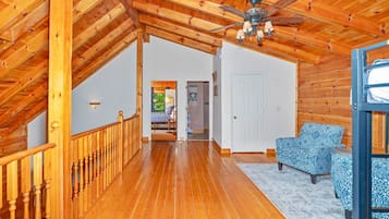 A wooden interior with a staircase, a ceiling fan, and patterned chairs.