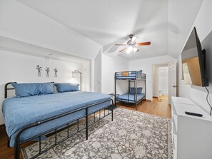 A bedroom with a bunk bed, a single bed, a ceiling fan, a television, and a patterned rug.
