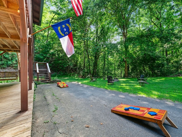 A wooden deck with a picnic table and a game board, surrounded by a forested area.