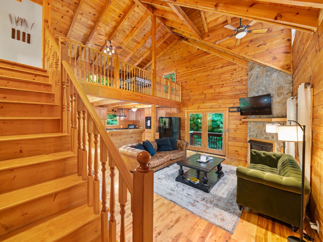 A wooden cabin interior with a staircase, a living room with a sofa and coffee table, a fireplace, and a television.