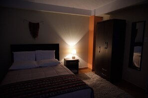 Una habitación de hotel con cama, mesita de noche con lámpara, armario y espejo en la pared.