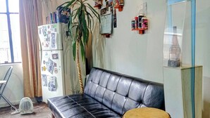 A room with a black leather sofa, a red drum, a refrigerator, a fan, and a wall decorated with photos and cans. - Beer and Beer (Valparaíso)