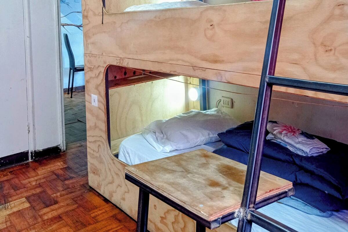 A bunk bed room with a wooden bunk bed, a small table, and a chair.