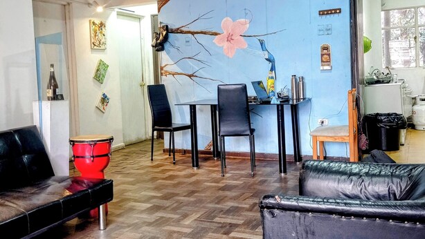A living room with a blue wall, a wooden floor, a black leather sofa, a red drum, and a dining table with chairs. - Beer and Beer (Valparaíso)