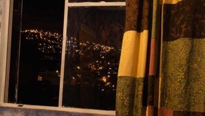 A room with a bed, a window with curtains, and a view of a cityscape at night. - Beer and Beer (Valparaíso)