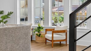A modern living room with a large window, a wooden chair, a textured sofa, and a woven side table with a plant.