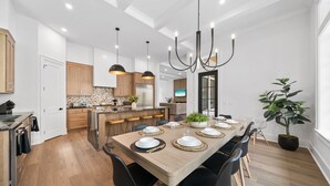 A modern kitchen with wooden cabinets, a central island, and a dining area with a long table set for six.