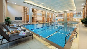 Una piscina interior con sillas de descanso y toallas, separadores de madera y suelo de baldosas.