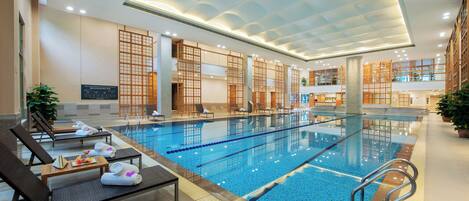 An indoor swimming pool with lounge chairs and towels, wooden partitions, and a tiled floor.