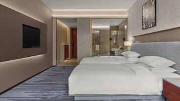 Une chambre d’hôtel moderne dotée d’un grand lit, d’une télévision à écran plat, d’une douche à l’italienne et d’une salle de bain avec un miroir et un lavabo.