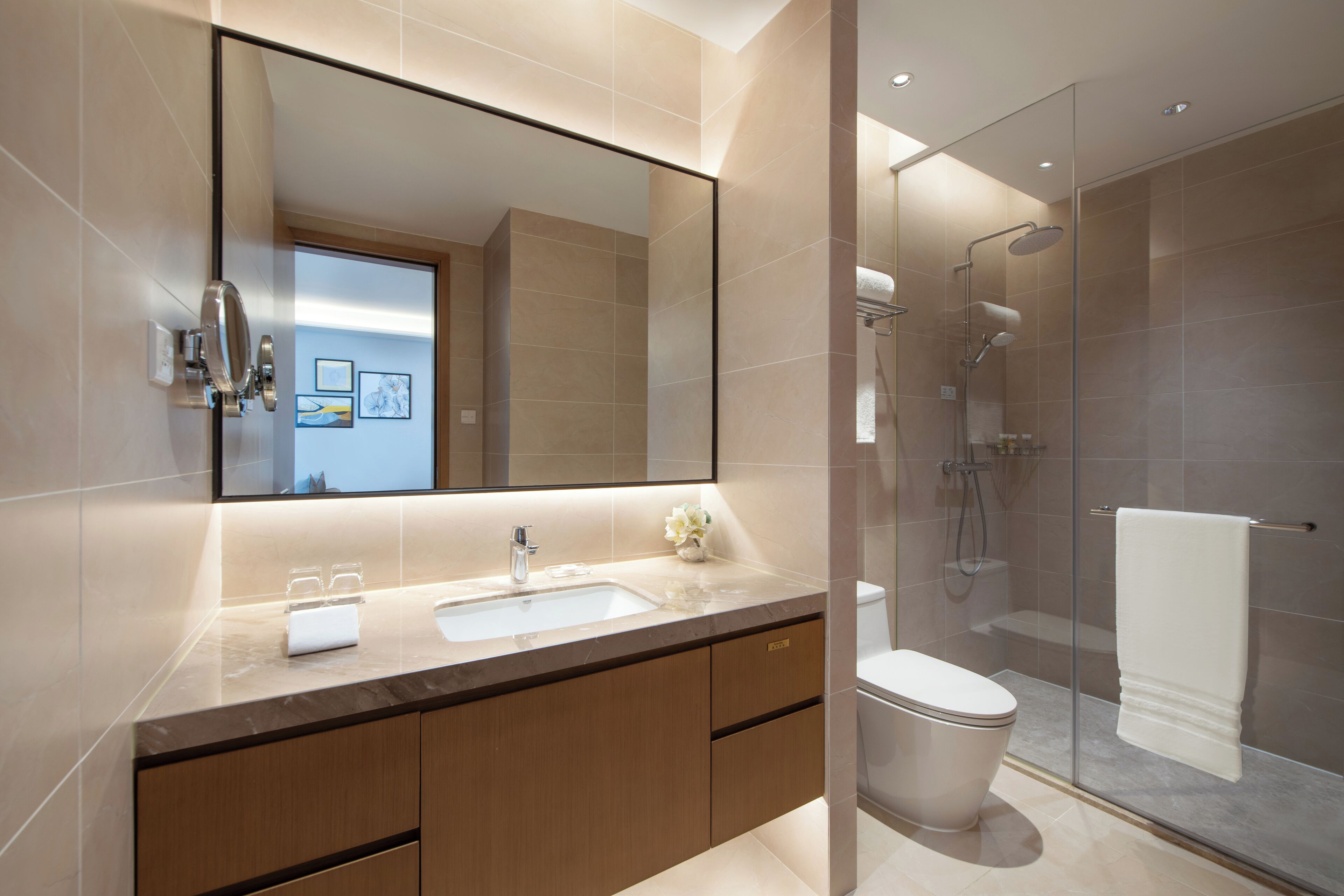 Un baño moderno con un espejo grande, un lavamanos, un inodoro y una zona de ducha con paredes de vidrio.