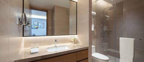 A modern bathroom with a large mirror, a sink, a toilet, and a glass-enclosed shower area.