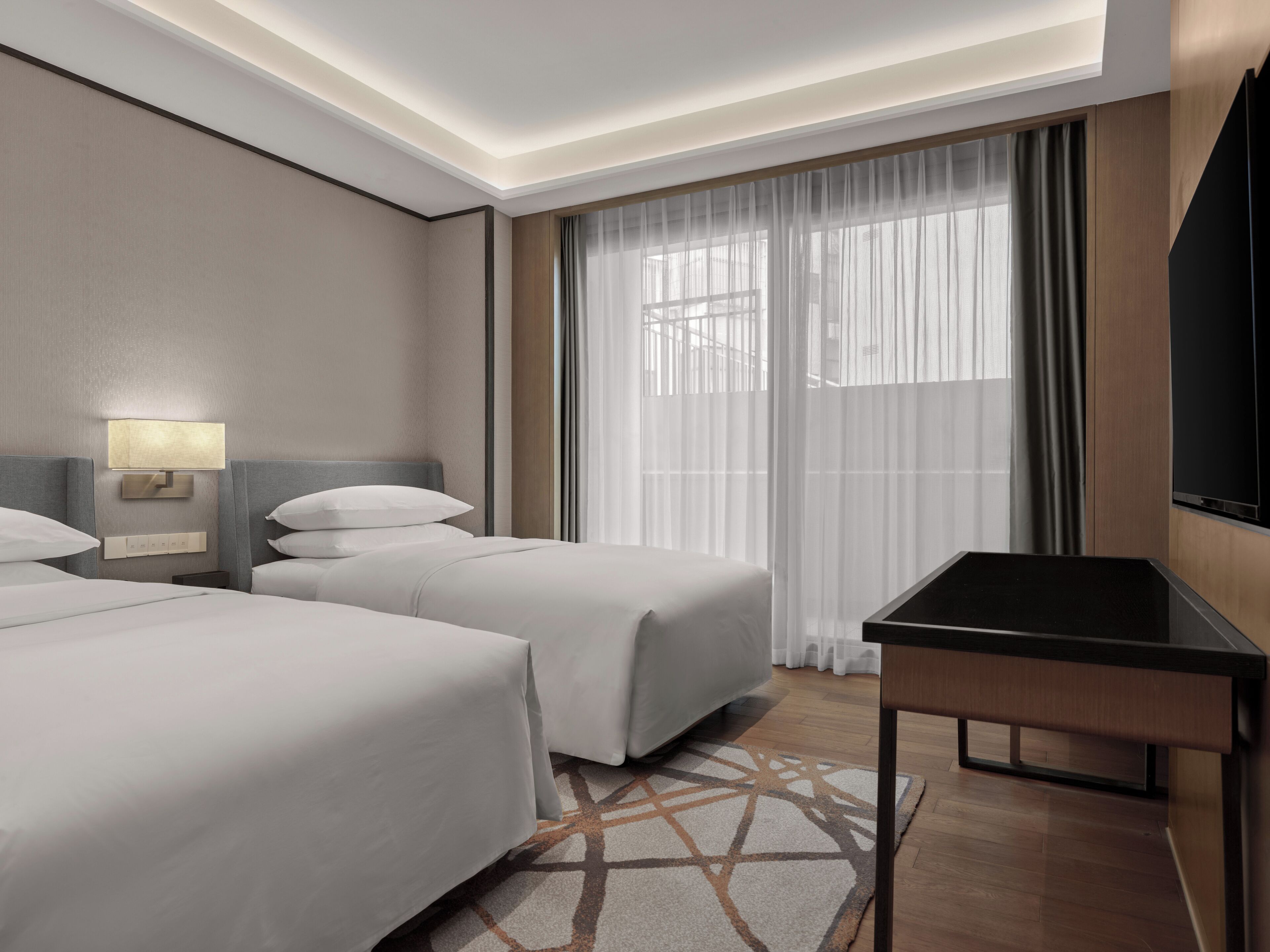 Une chambre d’hôtel avec deux lits, un bureau, une télévision et une fenêtre avec des rideaux.