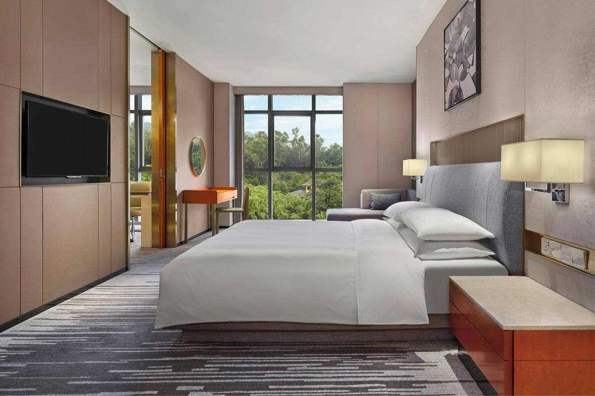 Ein modernes Hotelzimmer mit einem großen Bett, einem Flachbildfernseher, einem Schreibtisch und Blick ins Freie.