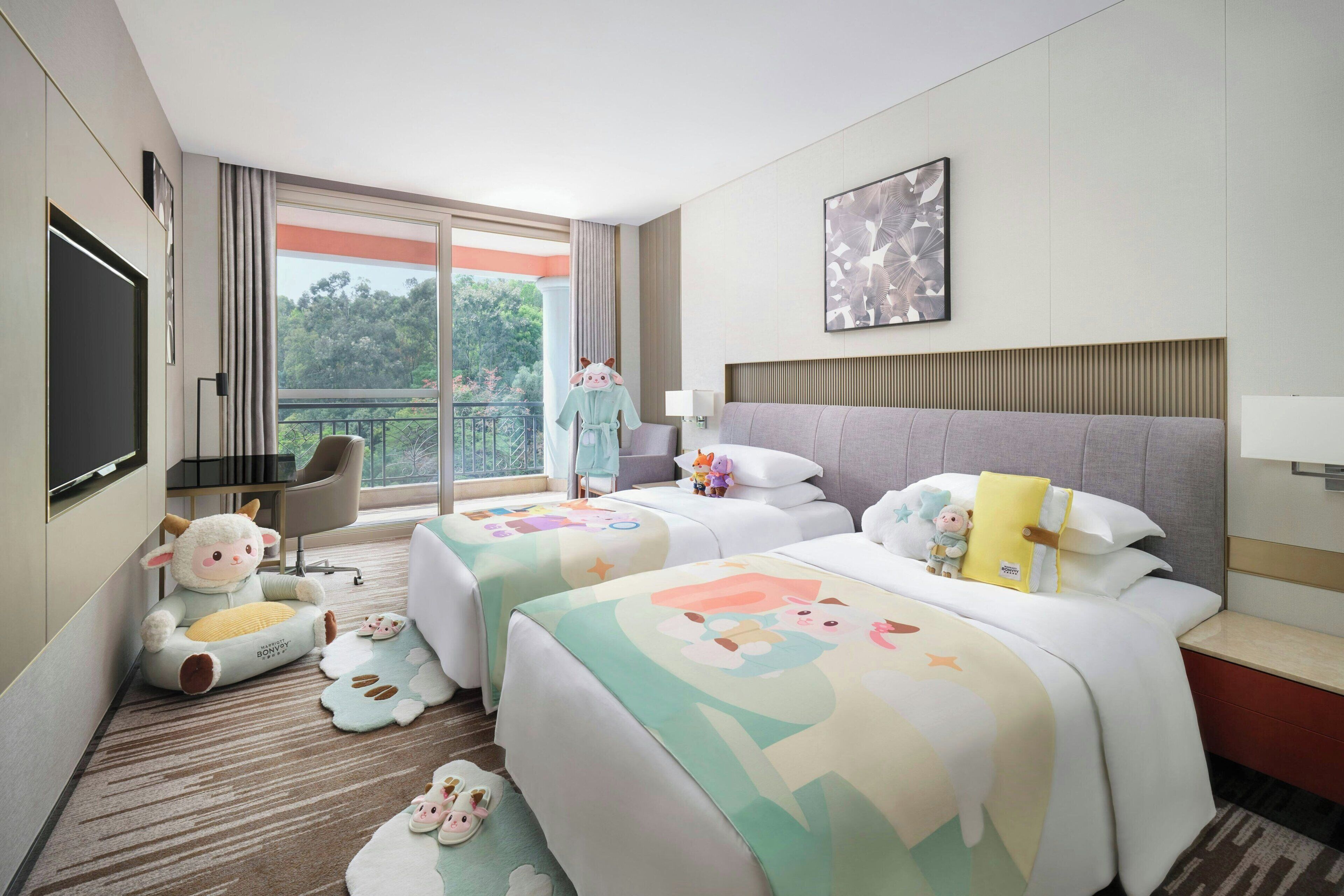 A hotel room with two beds, a TV, a balcony, and a view of trees.