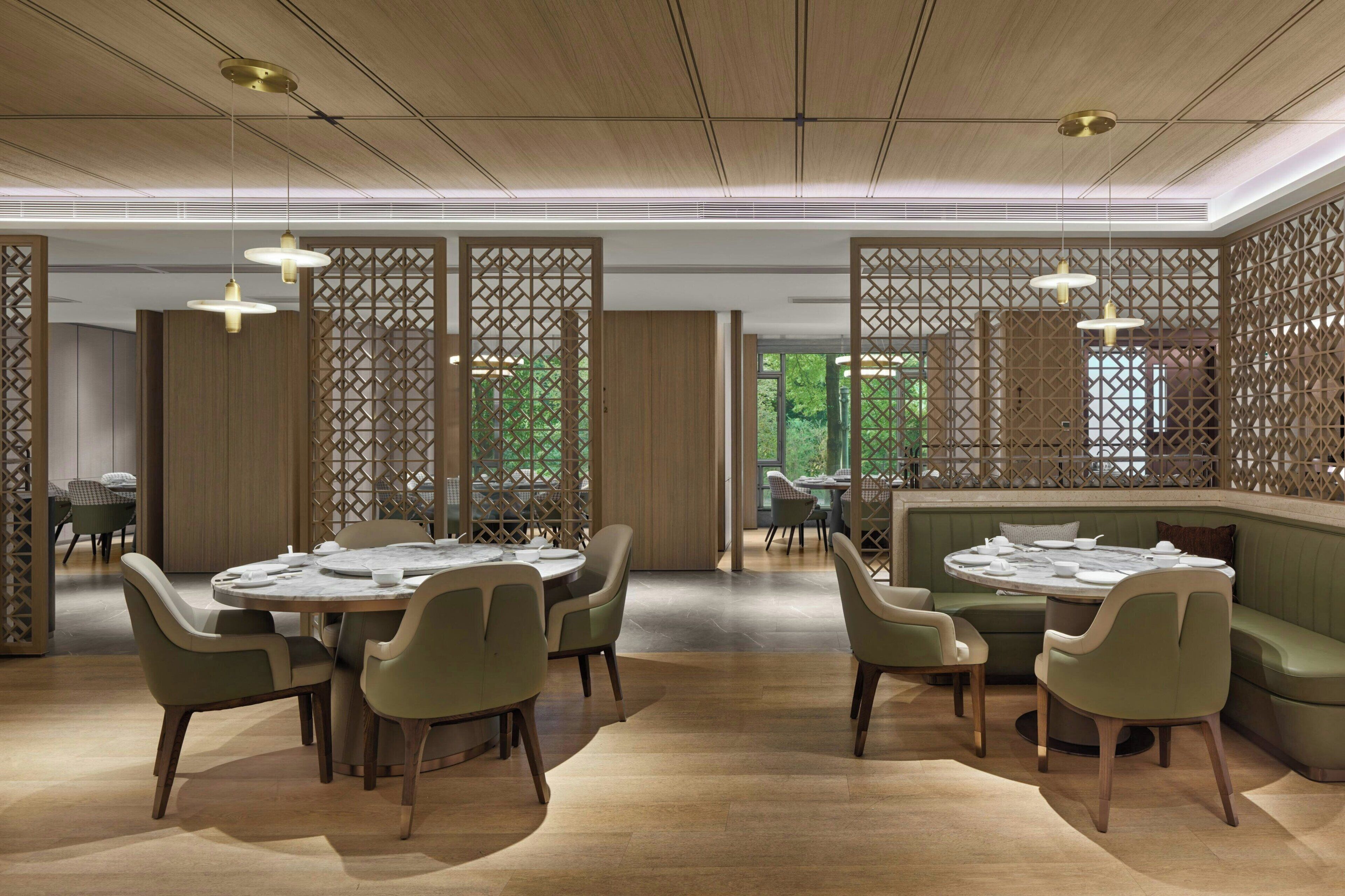 A modern dining area with round tables, green upholstered chairs, and pendant lighting.