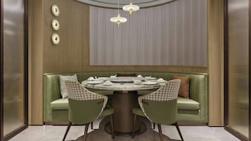A dining area with a round table, two chairs, a green sofa, and a ceiling light fixture.