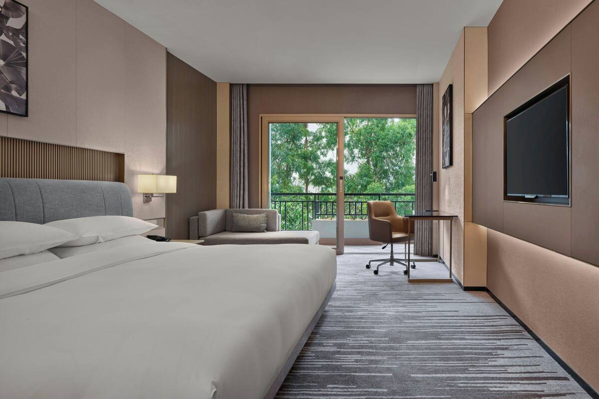 Ein Hotelzimmer mit einem großen Bett, einem Schreibtisch, einem Sessel und einem Fernseher.