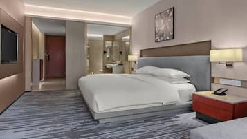 Una habitación de hotel moderna con una cama grande, lámparas de noche, un televisor de pantalla plana y un baño visible a través de una puerta abierta.