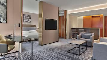 Une chambre d’hôtel moderne équipée d’un lit, d’un bureau, d’une télévision et d’un coin salon avec un canapé et des fauteuils.
