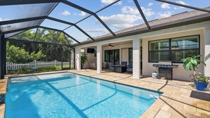 Una piscina exterior techada con zona de patio, una parrilla y una cerca de piquetes blancos.