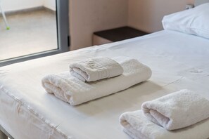 Een netjes opgemaakt bed met twee witte handdoeken erbij.