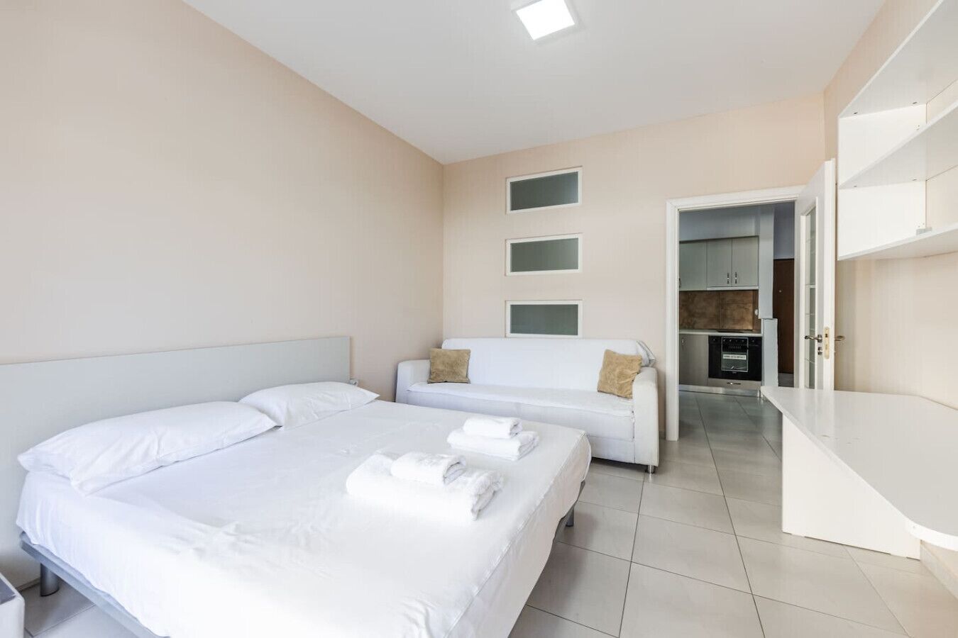 A hotel room with two beds, a sofa, a kitchenette, and a bathroom.