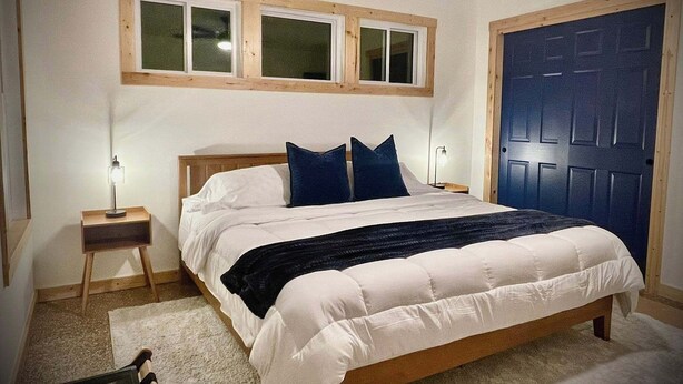 Un dormitorio con una cama, dos mesitas de noche, una ventana y una puerta.