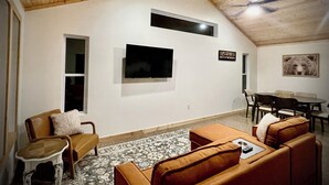 Una sala de estar acogedora con techo alto, un televisor de pantalla plana en la pared, una mesa de comedor con sillas y una alfombra estampada en el suelo.