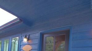Una casa azul con puerta principal oscura, un cartel de bienvenida y una lámpara sobre la puerta.