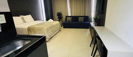 Habitación de hotel compacta con cama, pequeña kitchenette, zona de estar y televisión.