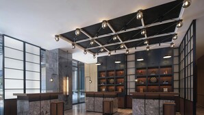Un vestíbulo moderno con suelo de mármol, un mostrador de recepción y un techo con vigas a la vista y luces colgantes.