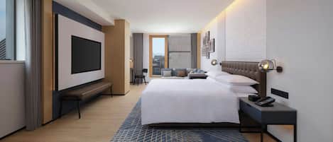 A modern hotel room with a large bed, a TV, a desk with a lamp, and a city view.