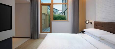 A modern hotel room with a large bed, a television, a window with curtains, and a view of the outside.