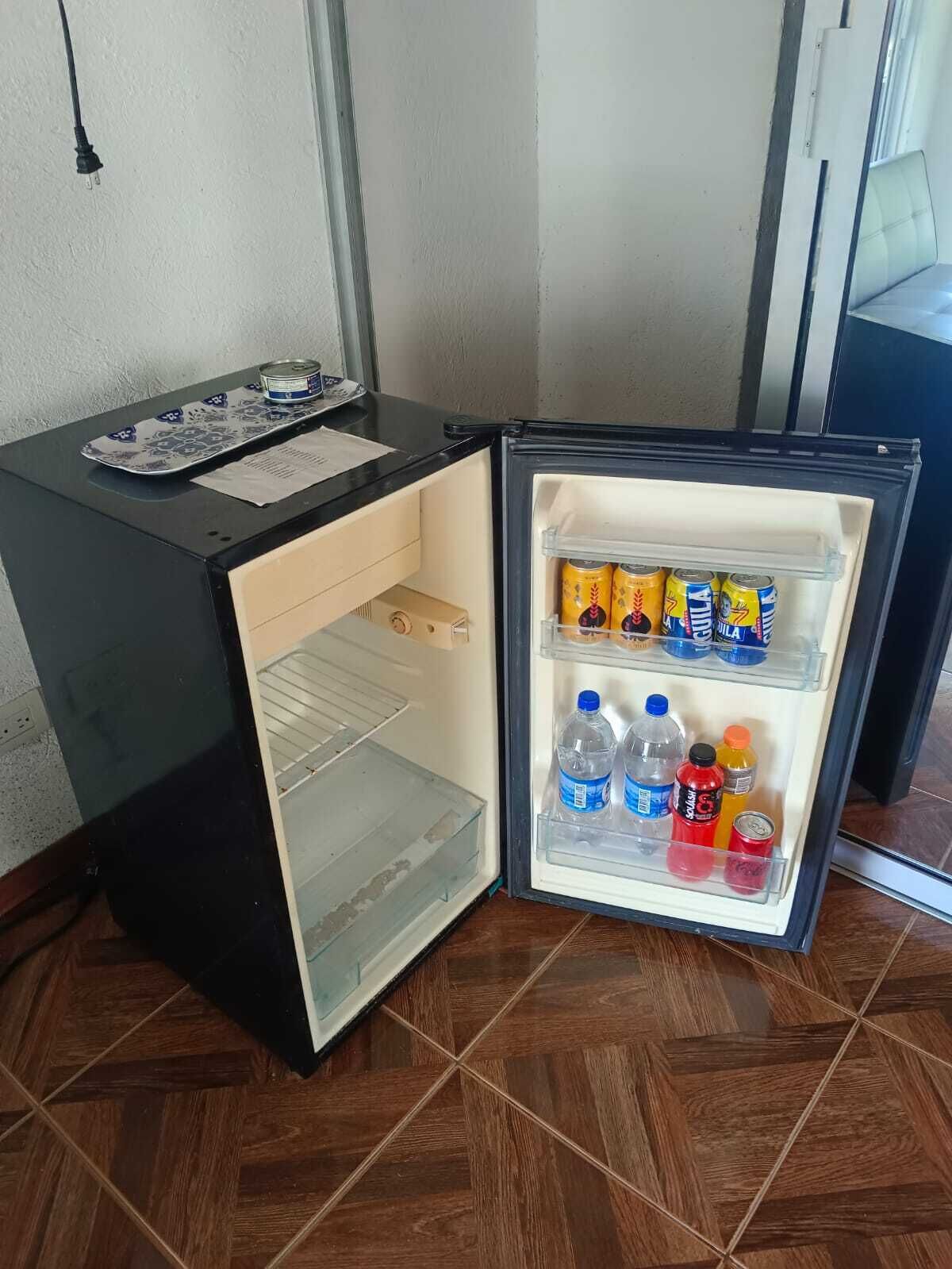 A compact refrigerator with a freezer compartment, containing beverages and a can.