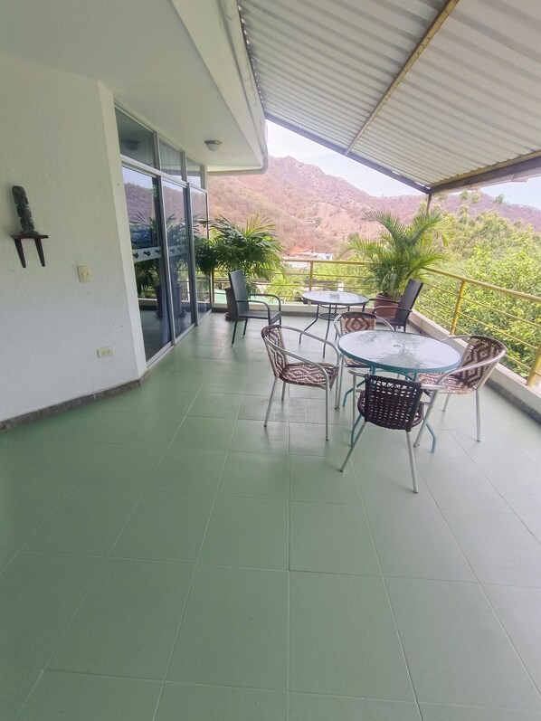 A covered balcony with a table and chairs, potted plants, and a view of a mountainous landscape. - MAUKA OASIS Taganga  (Santa Marta)