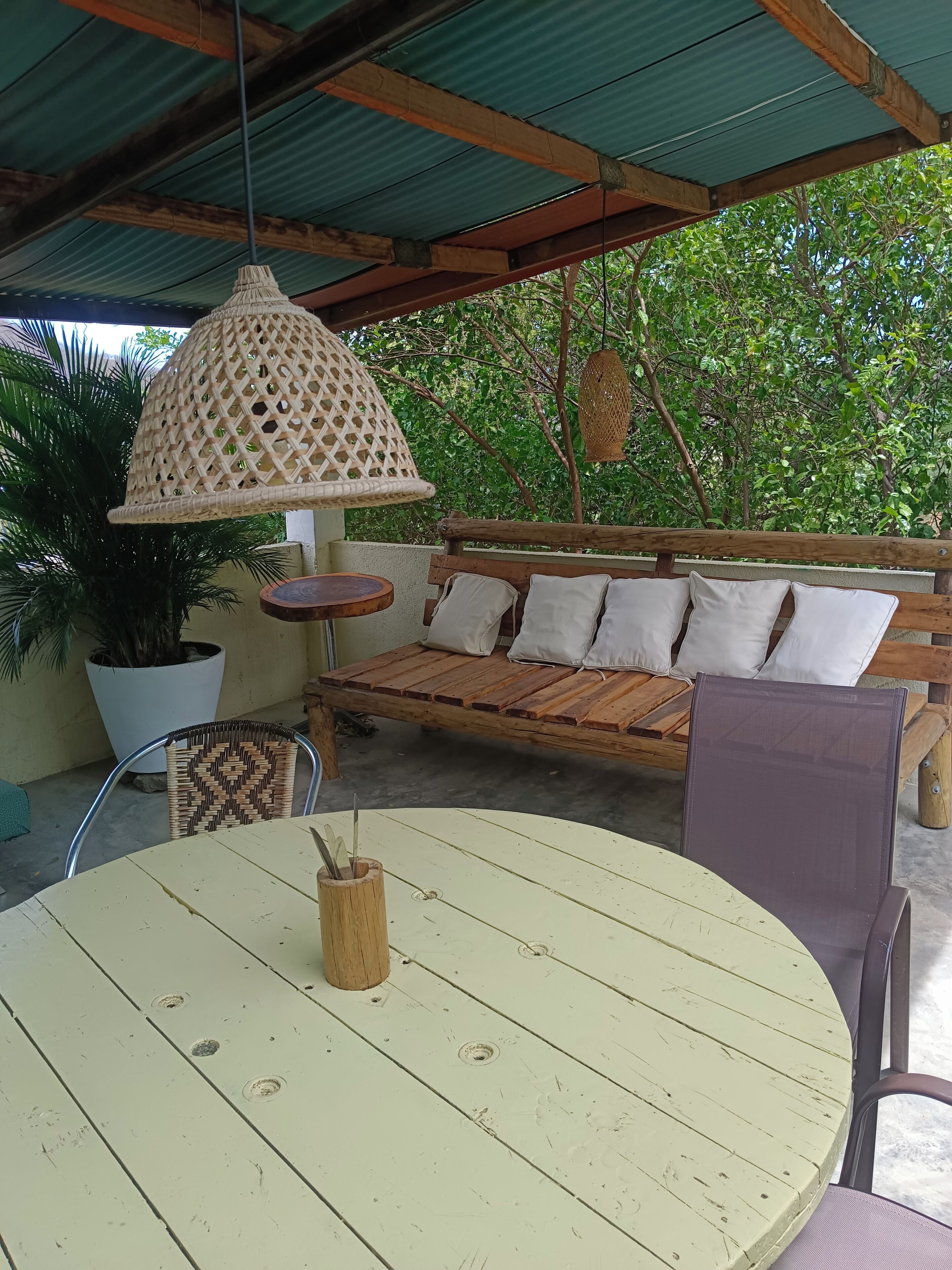 An outdoor seating area with a round table, a bench with cushions, and a hanging light fixture.