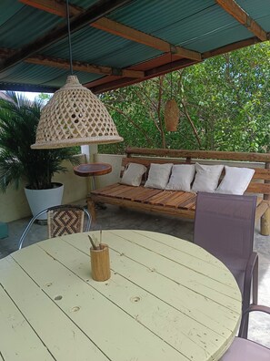 An outdoor seating area with a round table, a bench with cushions, and a hanging light fixture. - MAUKA OASIS Taganga  (Santa Marta)
