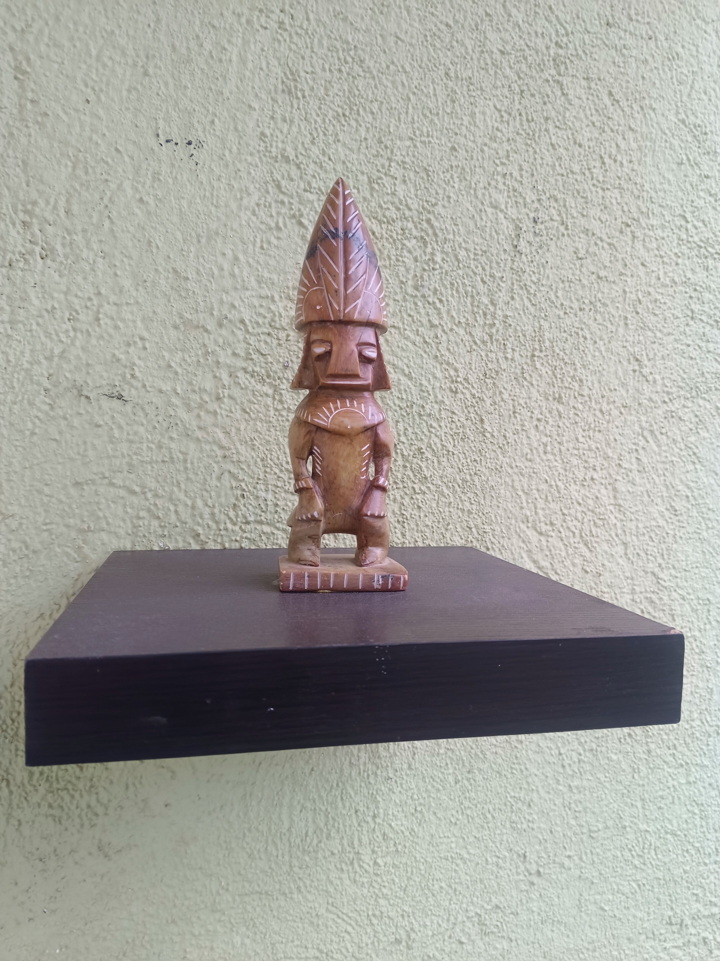 A wooden statue on a dark shelf against a textured wall.