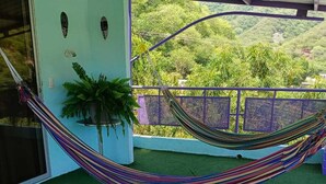 A hammock on a balcony with a view of green hills, a potted plant, and a straw hat on a table. - MAUKA OASIS Taganga  (Santa Marta)