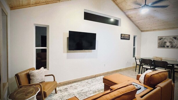Una sala de estar con techo alto, un televisor de pantalla plana montado en la pared, un comedor con mesa y sillas, y un cartel en la pared.