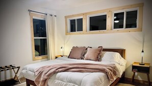 Un dormitorio con una cama grande, dos mesitas de noche, una ventana y un cabecero de madera.